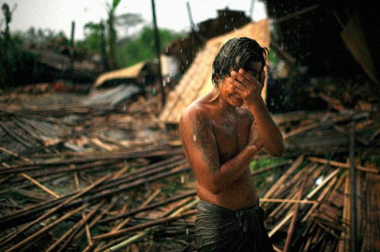Myanmar'da fakir bir genç, evinin yıkıntılarının yanında dikiliyor ve yağmur...